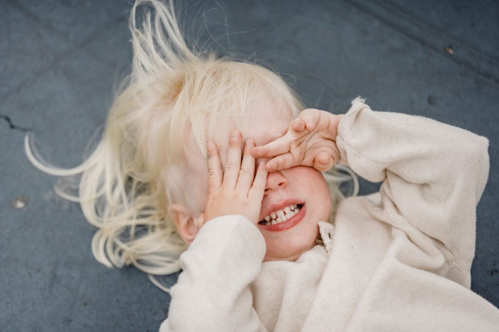 Blond dziecko leżące z dłońmi zasłaniającymi oczy